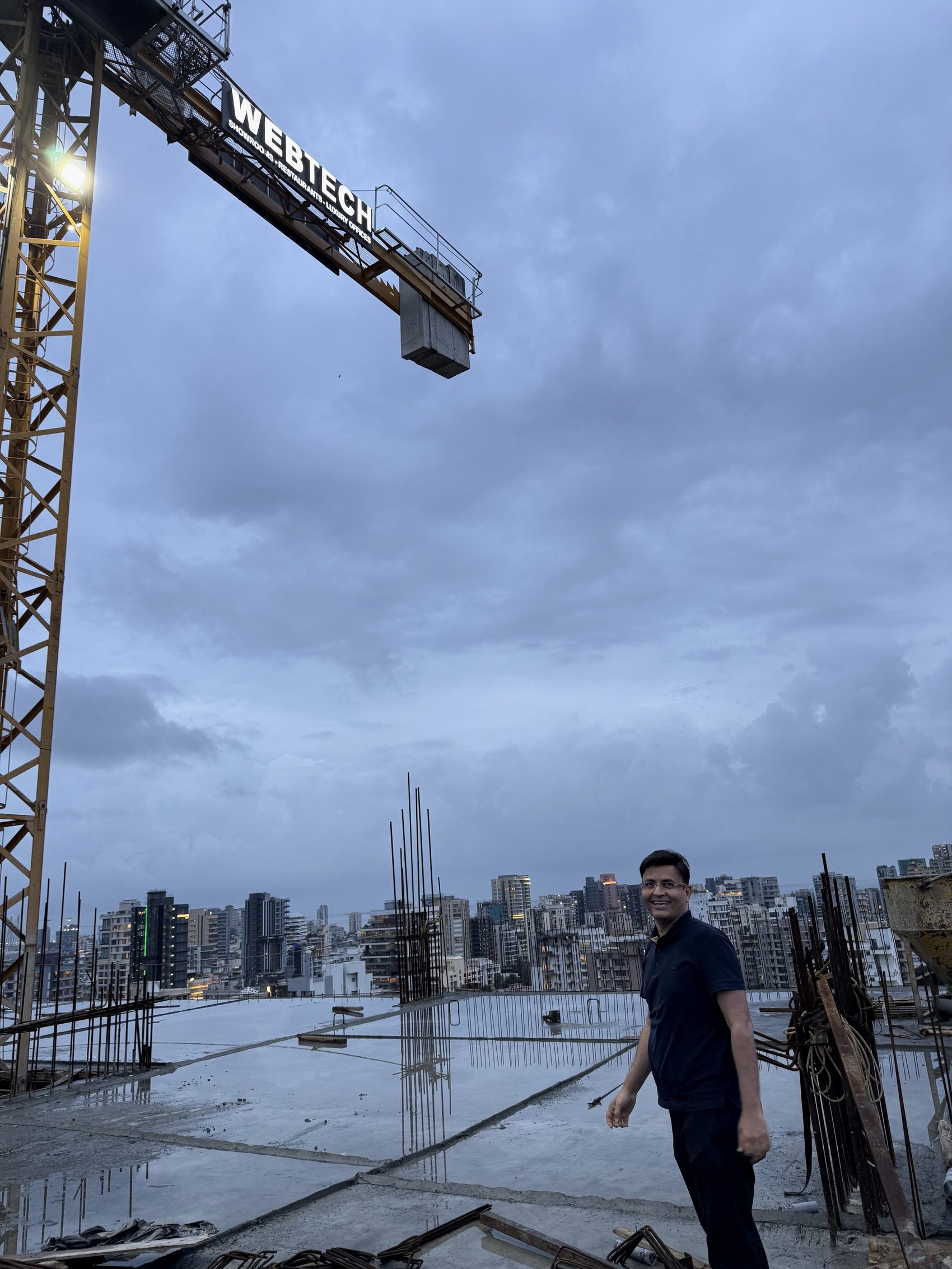 Amar Chhajed on site at a Webtech development, beneath the Webtech tower crane, the Mumbai skyline behind.
